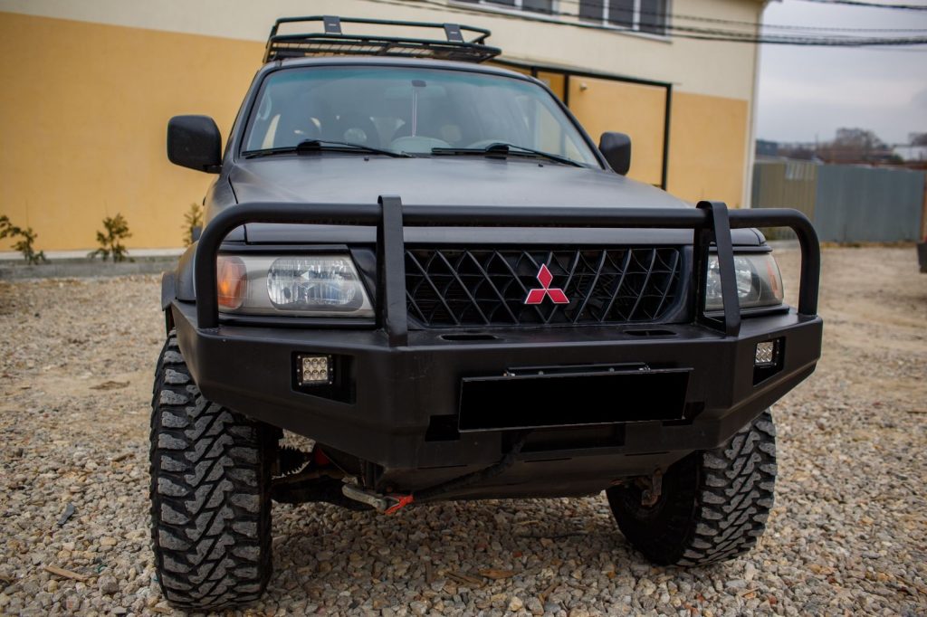 Бампер передний Mitsubishi Pajero Sport 1996-2008 с защитой фар, под ПТФ
